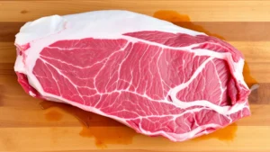 Raw beef short ribs with heavy marbling and white fat cap on wooden cutting board, trimmed silver skin visible, professional butcher preparation, natural lighting