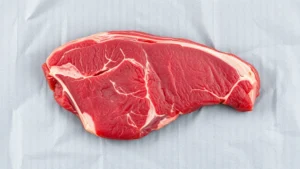 Close-up overhead shot of thinly sliced raw ribeye steak on parchment paper, partially frozen, ready for cooking on a griddle