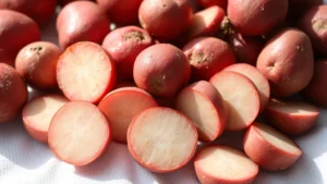 Close-up of fresh red potatoes with thin unblemished skin, some whole and some cut into quarters, arranged on a white kitchen towel with water droplets visible, natural daylight streaming across the surface
