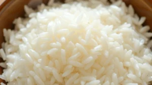 Close-up of perfectly cooked fluffy white rice in a ceramic bowl with individual grains clearly visible and separated, steam rising from surface, natural morning light