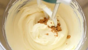 Close-up of creamy butter and brown sugar mixture being mixed in a stainless steel bowl with an electric mixer, showing fluffy pale texture